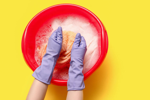 ゴム手袋の女性は,黄色の背景にプラスチック製の盆地で服を洗う - 写真・画像