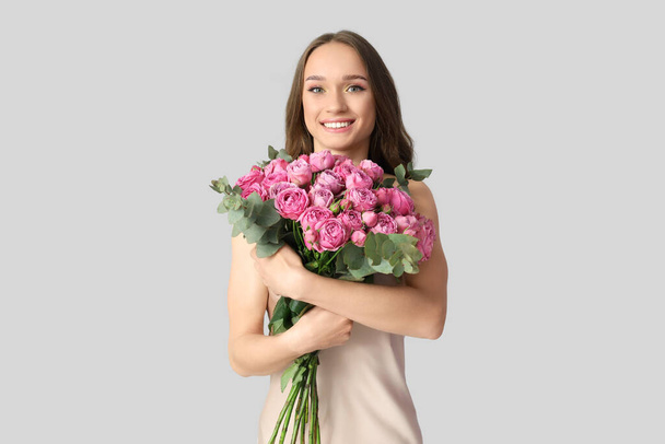 Krásná mladá žena s růžemi na světlém pozadí - Fotografie, Obrázek
