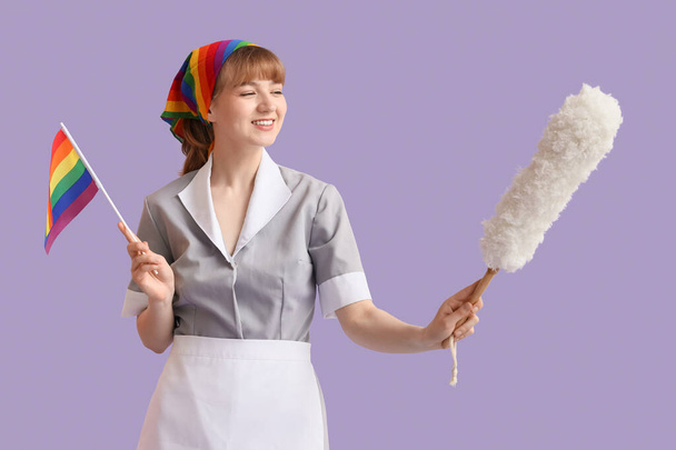 Young chambermaid with LGBT flag and pp-duster on lilac background - Photo, Image