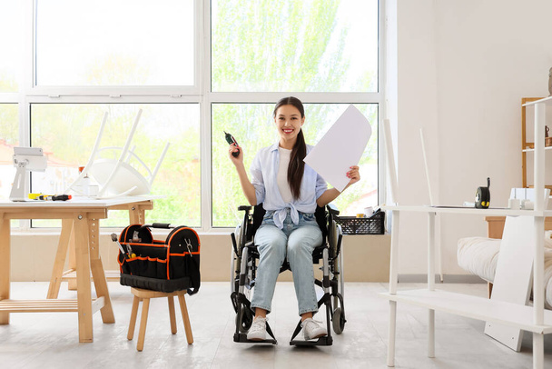 Молодая азиатка в инвалидной коляске с дрелью и ручной сборкой мебели на дому - Фото, изображение