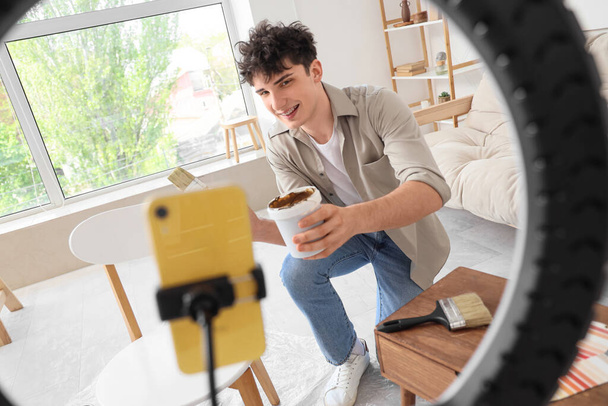 Blogger masculino con muebles de pintura de pincel mientras graba video en casa - Foto, imagen