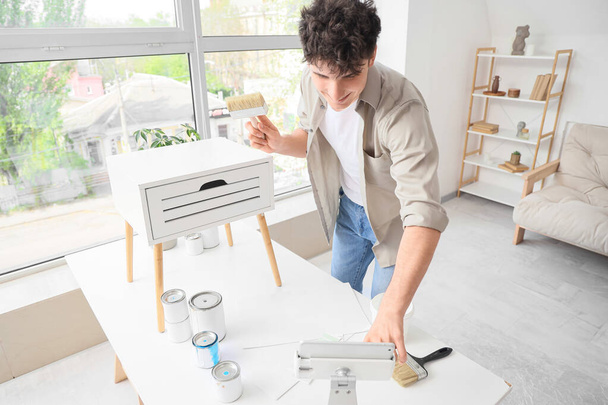 Hombre joven que usa tableta mientras pinta mesa en casa - Foto, imagen