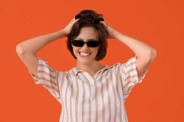 problémová mladá žena se slunečními brýlemi na oranžovém pozadí - Fotografie, Obrázek
