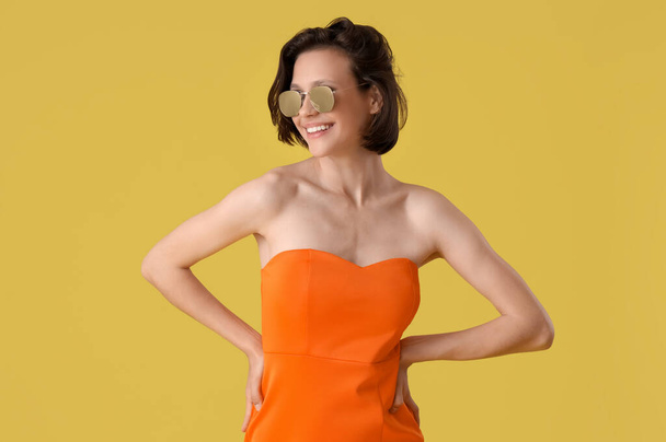 Pretty young woman with sunglasses on yellow background - Photo, Image