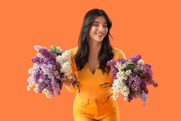 Bella giovane donna con fiori lilla su sfondo arancione - Foto, immagini