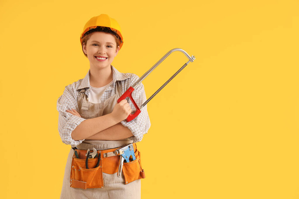 Joven carpintera femenina con sierra de arco sobre fondo amarillo. Fiesta del Día del Trabajo - Foto, imagen