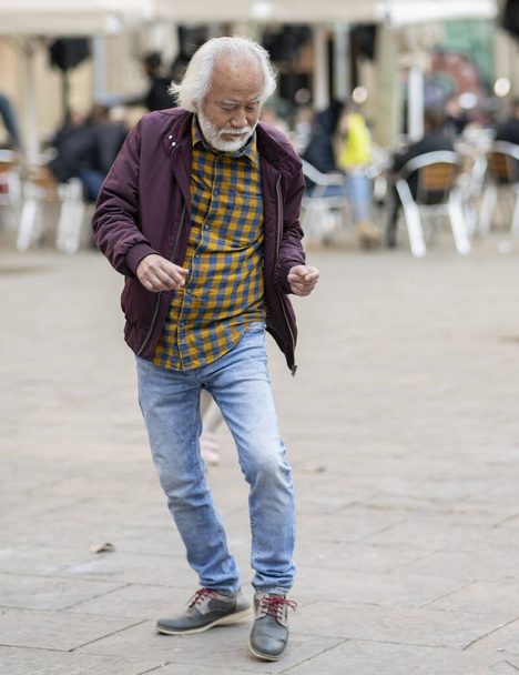 Starší pán radostně tančí sám na rušném náměstí, jeho temperamentní kroky vyjadřují svobodu a štěstí. - Fotografie, Obrázek