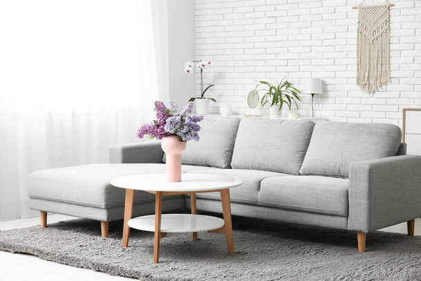 Elegante interno del soggiorno con mazzo di rami di lilla sul tavolino vicino al divano - Foto, immagini