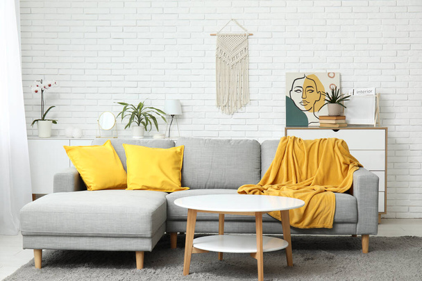 Wnętrze jasnego salonu z wygodną sofą, poduszkami i żółtą kratą - Zdjęcie, obraz
