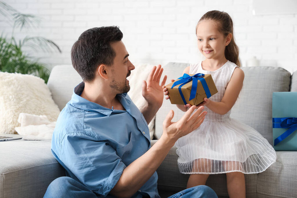 Küçük kız, oturma odasında babasına hediye veriyor. Babalar günü kutlaması. - Fotoğraf, Görsel