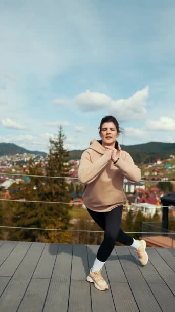 Mujer joven hace ejercicios matutinos en la terraza de un hotel con vistas a las montañas nevadas. El concepto de un estilo de vida saludable. Vídeo vertical - Imágenes, Vídeo