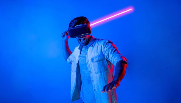 Hombre caucásico con gafas VR y gesto en movimiento sosteniendo la espada. Gamer utilizando futuros auriculares de realidad virtual digital o innovación futurista para entrar en el mundo meta o jugar juego de acción. Desviación. - Foto, imagen
