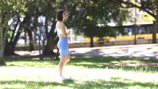Nainen kävelee puistossa keltainen bussi taustalla. Hänellä on sininen toppi ja siniset shortsit. - Materiaali, video