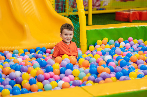 Egy boldog kisfiú játszik egy száraz medencében színes golyókkal. Játék szórakoztató központ gyerekeknek. Aktív pihenés - Fotó, kép