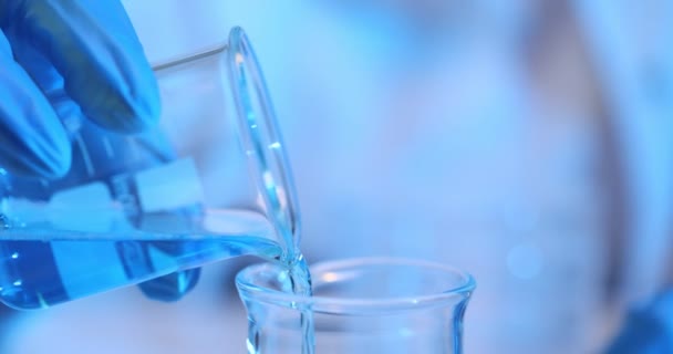Lateksikäsineiden tutkija kaataa nestettä lasilasiin laboratoriossa hidastettuna. Laboratorion työntekijä valmistaa reagenssin kokeeseen - Materiaali, video