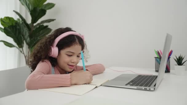 Side view of girl wearing headphone and doing homework in self study. Happy attractive schoolgirl writing at notebook while searching about programing system and writing engineering prompt. Pedagogy. - Footage, Video