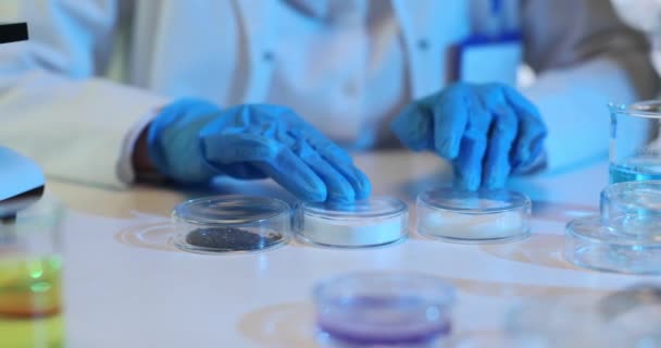 Lateks eldivenli laboratuvar çalışanı, yavaş çekim numuneleriyle Petri kabının yerini değiştiriyor. Uzman, iş yerinde deneyler için örnekler hazırlıyor - Video, Çekim