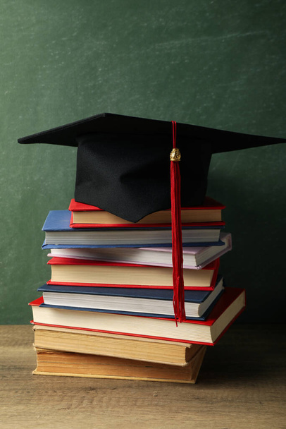Καπέλο αποφοίτησης με βιβλία σε τραπέζι σε σκούρο φόντο. - Φωτογραφία, εικόνα