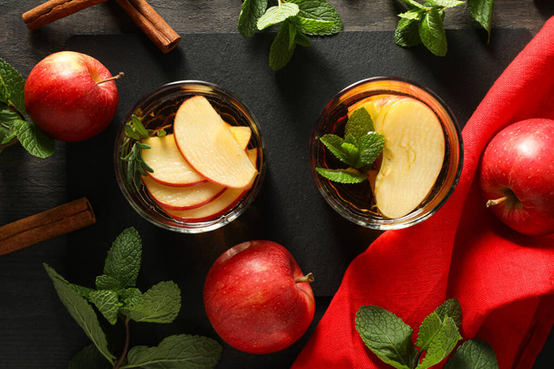 Очки с яблочным сидр, листья мяты и красные яблоки на темном деревянном фоне, вид сверху - Фото, изображение