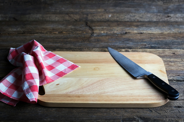 Placa de corte vazia com uma faca de corte afiada e guardanapo em uma mesa de madeira grunge angustiada
 - Foto, Imagem