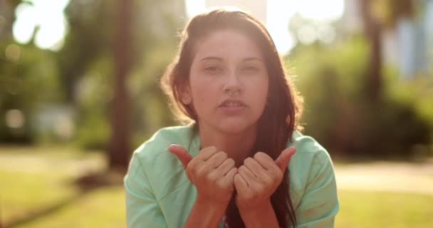 Casual young woman giving thumbs up and smiling to camera while adjusting hair outdoors - Filmagem, Vídeo