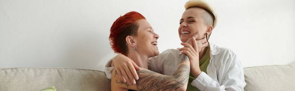 Two women with short hair share a warm hug on a cozy couch, expressing love, comfort, and connection. - Photo, Image