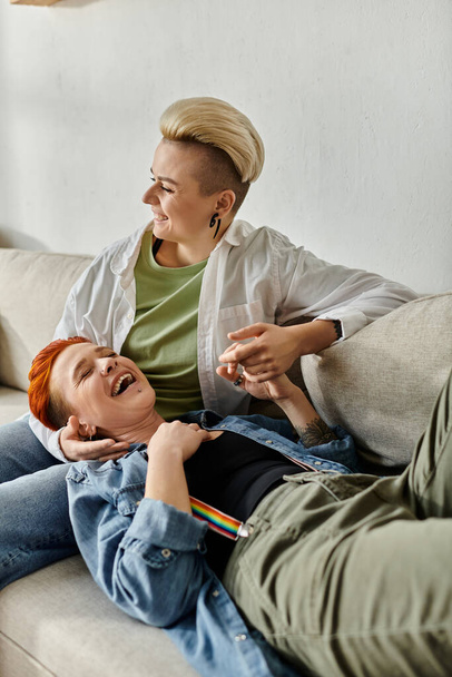 Лесбійська пара з коротким волоссям сидить разом на дивані, розділяючи момент сміху і радості. - Фото, зображення