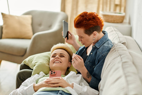 Δύο γυναίκες με κοντά μαλλιά κάθονται σε έναν καναπέ, πνιγμένες στη συζήτηση, επιδεικνύοντας αγάπη και σύνδεση.. - Φωτογραφία, εικόνα