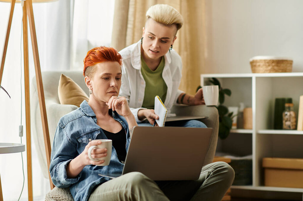 Un couple de lesbiennes aux cheveux courts travaillant sur un ordinateur portable dans un salon confortable, se concentrant intensément sur leurs tâches. - Photo, image