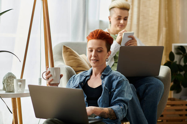 Zwei Frauen mit kurzen Haaren sitzen auf einer bequemen Couch, jede konzentriert auf ihren Laptops, vertieft in ihre Online-Welt. - Foto, Bild