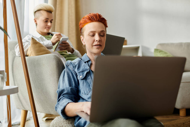 Két rövid hajú nő ül a kanapén, belemerülve egy laptopba otthon.. - Fotó, kép