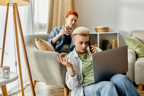 Um casal de lésbicas em um sofá usando um laptop e falando ao telefone. - Foto, Imagem