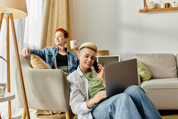 Egy leszbikus pár a kanapén pihen, kávét kortyolgat és laptopot használ.. - Fotó, kép
