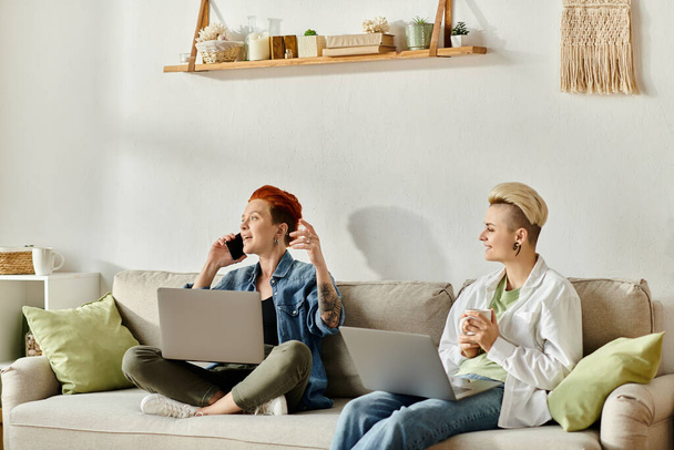 Dos mujeres, una con el pelo corto, sentadas en un sofá con ordenadores portátiles, enfocadas y comprometidas en su trabajo o proyecto. - Foto, Imagen