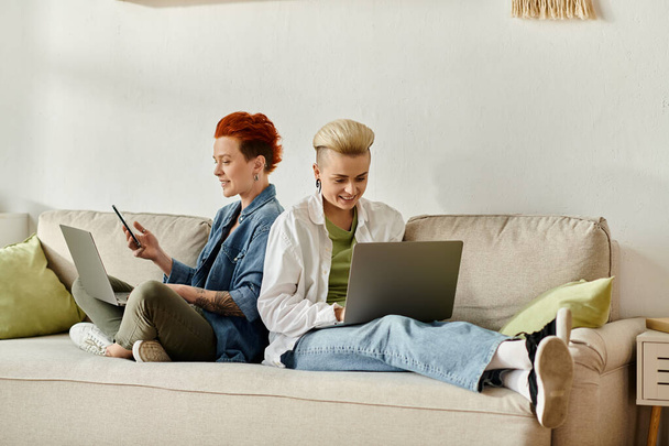 Дві жінки з коротким волоссям сидять на дивані, зачаровані ноутбуками в затишній домашній обстановці. - Фото, зображення