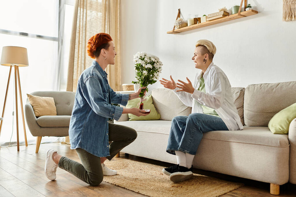 Женщина дарит цветы своему партнеру, сидящему дома на диване, делая предложение - Фото, изображение