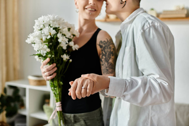 λεσβιακό ζευγάρι που κρατάει λουλούδια και δείχνει τη βέρα του σε ένα άνετο σαλόνι. - Φωτογραφία, εικόνα