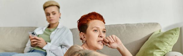 Женщина с короткими волосами сидит на уютном диване, поглощенном мобильным телефоном. - Фото, изображение