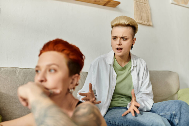Δύο γυναίκες με κοντά μαλλιά κάθονται σε έναν καναπέ, ασχολούνται με συναισθηματική συνομιλία στο σπίτι. - Φωτογραφία, εικόνα