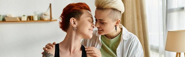 Deux femmes aux cheveux courts partagent un câlin sincère dans leur salon confortable, exprimant amour et unité. - Photo, image