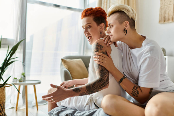 Дві вихрові жінки з татуюваннями сидять близько на затишному дивані в стильній вітальні. - Фото, зображення