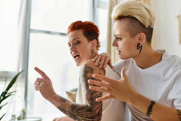 Zwei tätowierte Frauen liefern sich in einem stilvollen Wohnzimmer einen hitzigen Streit. Kurze Haare, offensichtlicher LGBT-Lebensstil. - Foto, Bild