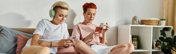 Dva mladí muži sedící na posteli, zabraní do společného hraní her na smartphone. - Fotografie, Obrázek