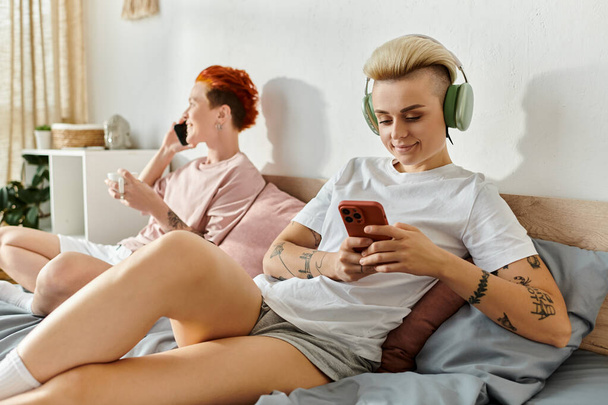 Двоє людей, лесбійська пара, сидить на ліжку і слухає музику з навушниками у своїй спальні. - Фото, зображення
