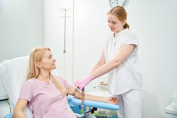 Nainen vierailee terveyskeskuksessa luovuttaakseen laskimon verinäytteen vitamiinien ja mikroelementtien puutteiden testaamiseksi kehossa, terveystarkastus - Valokuva, kuva