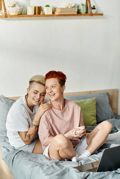Zwei Frauen, ein lesbisches Paar, sitzen auf einem Bett mit Laptop und konzentrieren sich konzentriert auf ihre Arbeit im Komfort ihres Schlafzimmers. - Foto, Bild