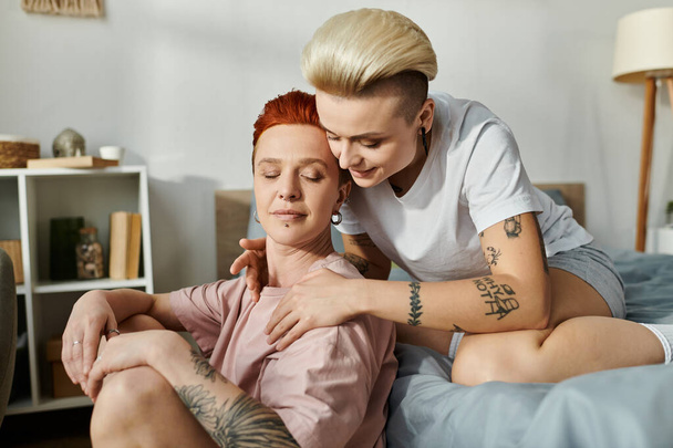 Лесбийская пара с короткими волосами тепло обнимает друг друга, лежа на кровати, демонстрируя любовь и близость.. - Фото, изображение