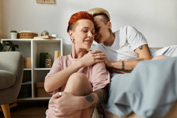 Un moment intime capturé comme deux femmes aux cheveux courts embrasser dans un câlin chaud sur un lit confortable dans une chambre. - Photo, image