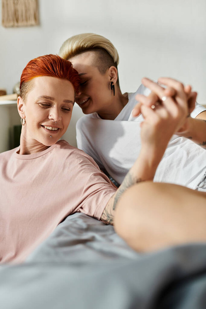Дві жінки з коротким волоссям лежать на ліжку, ділячись радісним моментом, коли вони посміхаються один одному в інтимній обстановці. - Фото, зображення