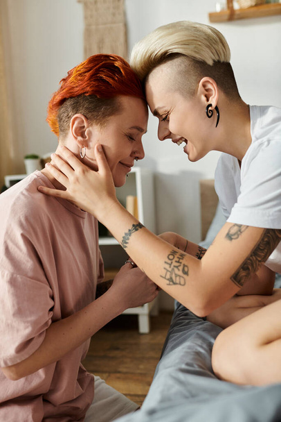 Lesbický pár s krátkými vlasy sedí na posteli, vyměňují si úsměvy a vyzařuje radost v jejich intimní ložnice nastavení. - Fotografie, Obrázek